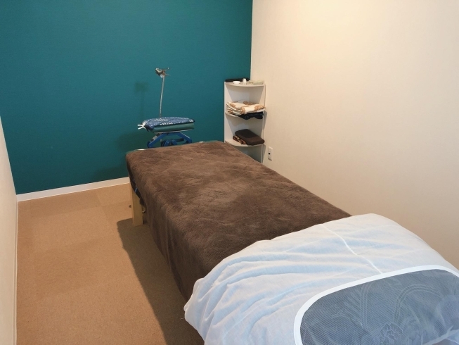 This is the individual room where the patient lies down to rest after treatment. It has a bed with a brown sheet and a white blanket with a gray sphere in the middle of the blanket. In the background, there is a corner cabinet that has some windows and at the head of the bed there is a blue pillow with a lining.